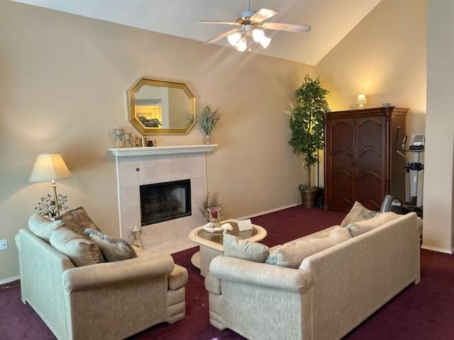 living room featuring dark colored carpet, ceiling fan, lofted ceiling, and a tiled fireplace