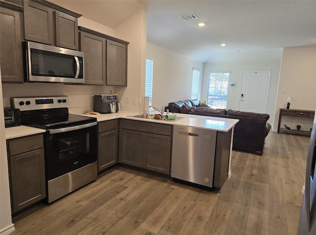 kitchen featuring dark brown cabinetry, sink, kitchen peninsula, wood-type flooring, and appliances with stainless steel finishes