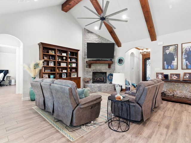 living room with beamed ceiling, a stone fireplace, high vaulted ceiling, and light wood-type flooring