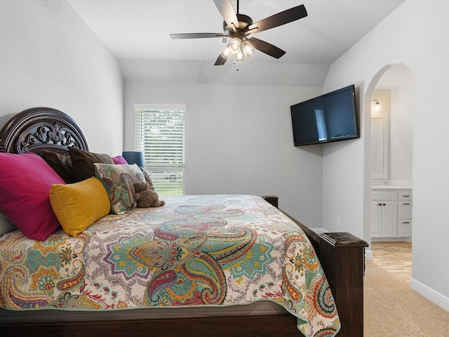 bedroom with vaulted ceiling, light colored carpet, ensuite bathroom, and ceiling fan