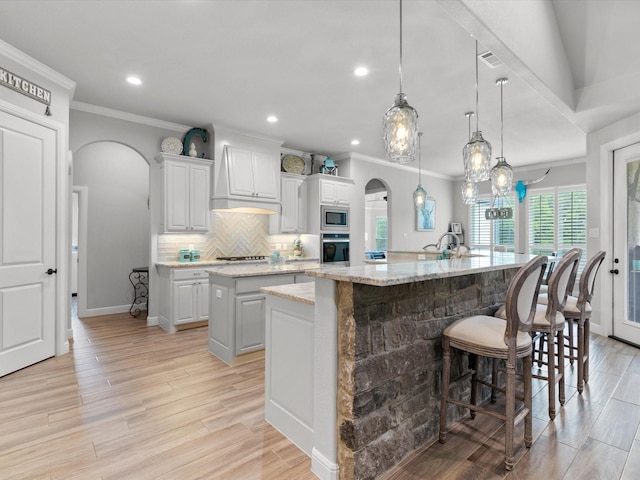 kitchen with light stone counters, decorative light fixtures, a large island with sink, appliances with stainless steel finishes, and white cabinets