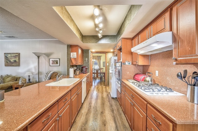 kitchen featuring light stone countertops, white appliances, a tray ceiling, sink, and light hardwood / wood-style flooring