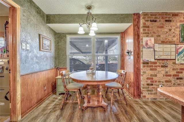 dining room with hardwood / wood-style floors, a textured ceiling, wooden walls, and a notable chandelier