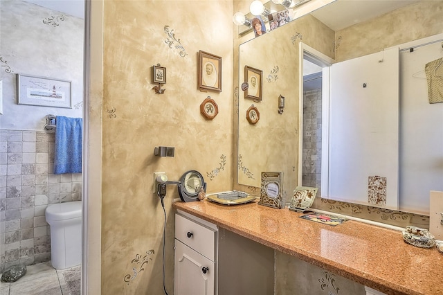 bathroom featuring vanity, toilet, and tile walls