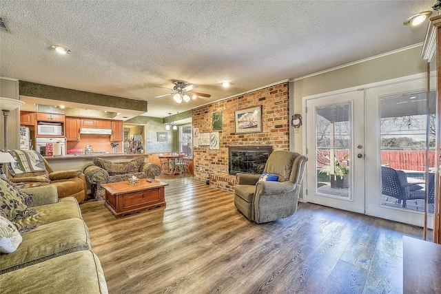 living room with french doors, hardwood / wood-style flooring, ceiling fan, a fireplace, and a textured ceiling