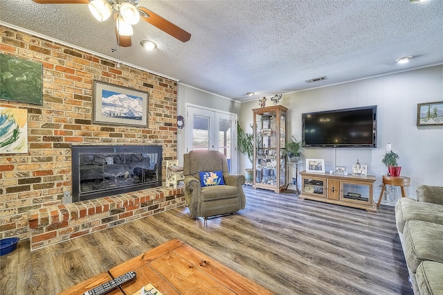 living room with french doors, crown molding, a brick fireplace, hardwood / wood-style flooring, and a textured ceiling