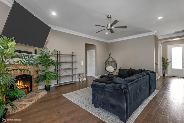 living room featuring dark hardwood / wood-style floors, ceiling fan, crown molding, and a fireplace