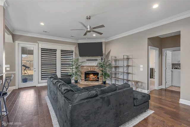 living room with ceiling fan, a stone fireplace, crown molding, and dark wood-type flooring