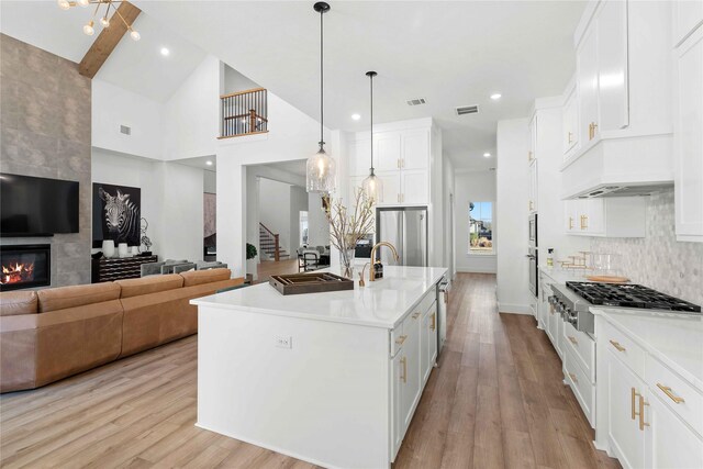 kitchen featuring a center island with sink, appliances with stainless steel finishes, decorative light fixtures, beam ceiling, and white cabinetry