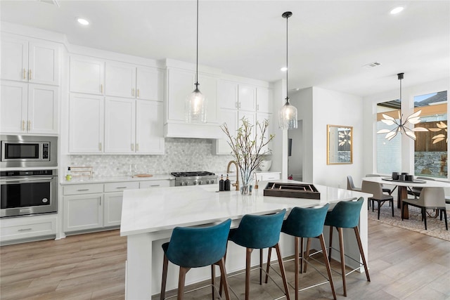 kitchen featuring white cabinetry, stainless steel appliances, a kitchen island with sink, and pendant lighting