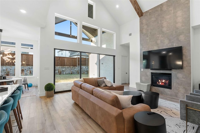 living room with a tile fireplace, beam ceiling, a towering ceiling, and light hardwood / wood-style floors