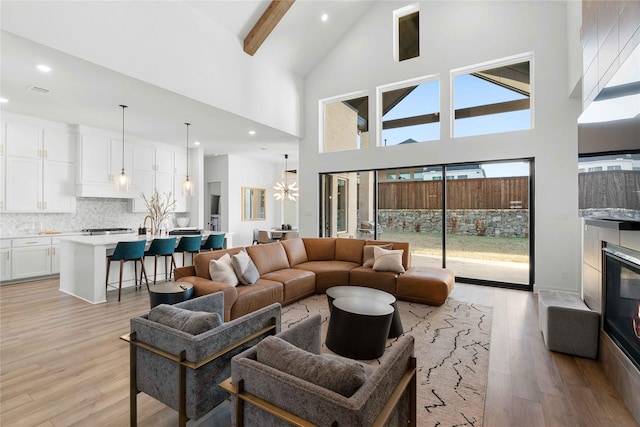 living room with beam ceiling, an inviting chandelier, a towering ceiling, and light hardwood / wood-style flooring