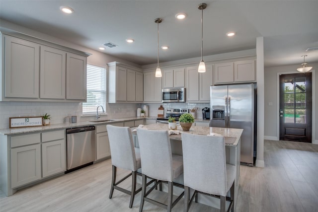 kitchen featuring appliances with stainless steel finishes, sink, pendant lighting, light hardwood / wood-style floors, and a kitchen island