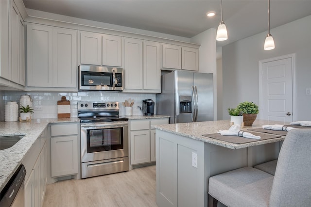 kitchen with light stone counters, stainless steel appliances, hanging light fixtures, and a breakfast bar area