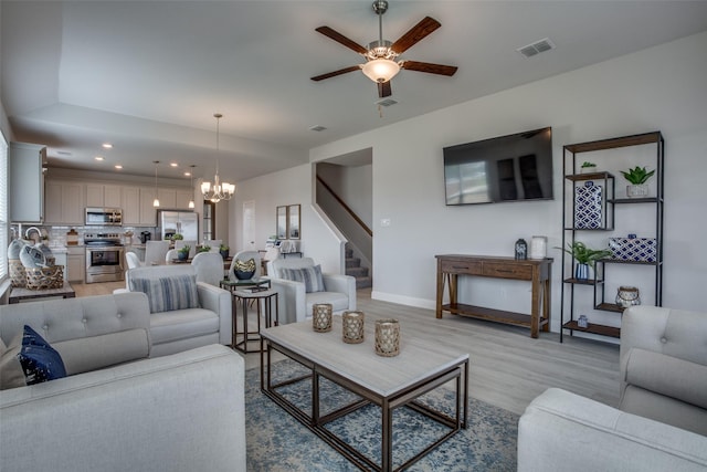 living room with ceiling fan with notable chandelier and light hardwood / wood-style floors