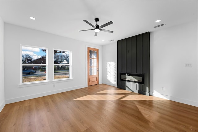 unfurnished living room featuring light wood-type flooring, a large fireplace, and ceiling fan