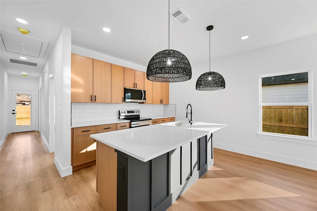 kitchen with backsplash, hanging light fixtures, light wood-type flooring, an island with sink, and stainless steel appliances