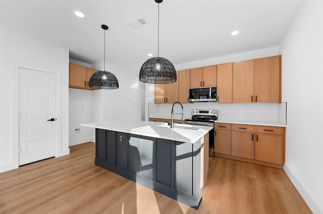 kitchen featuring a kitchen island with sink, sink, light hardwood / wood-style flooring, decorative light fixtures, and stainless steel appliances