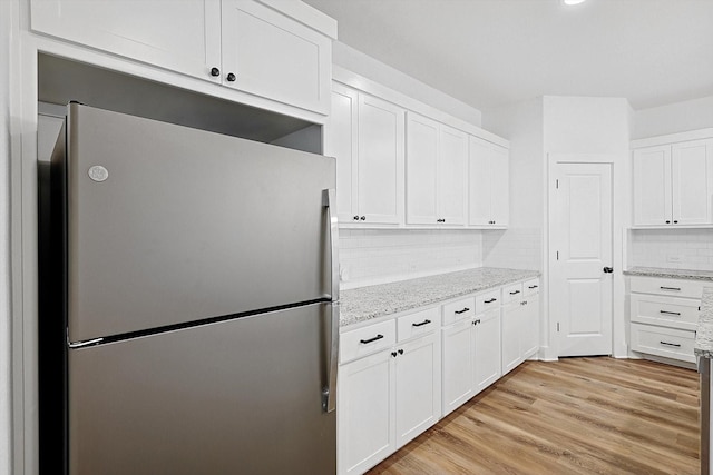 kitchen with tasteful backsplash, light stone counters, white cabinets, and stainless steel refrigerator