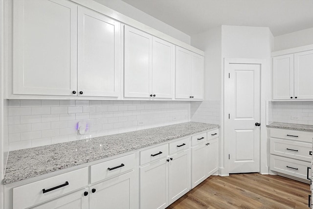 kitchen with white cabinetry, light stone countertops, light hardwood / wood-style floors, and decorative backsplash