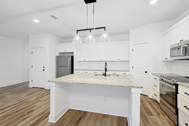 kitchen featuring an island with sink, stainless steel appliances, a sink, and decorative light fixtures