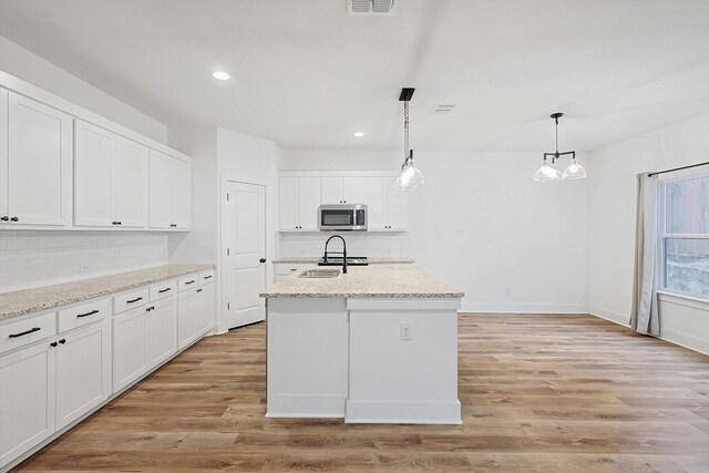 kitchen with pendant lighting, sink, white cabinetry, a center island with sink, and light wood-type flooring