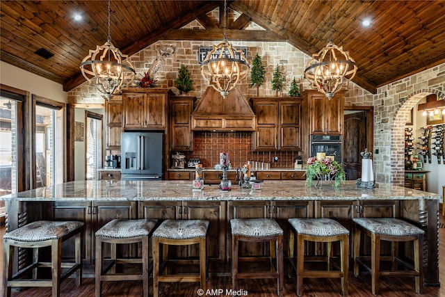 kitchen featuring a large island with sink, high quality fridge, a chandelier, and a kitchen bar