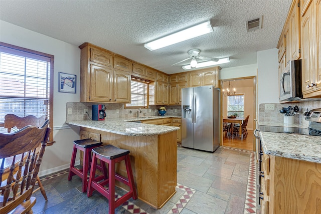 kitchen with kitchen peninsula, appliances with stainless steel finishes, a kitchen breakfast bar, tasteful backsplash, and ceiling fan