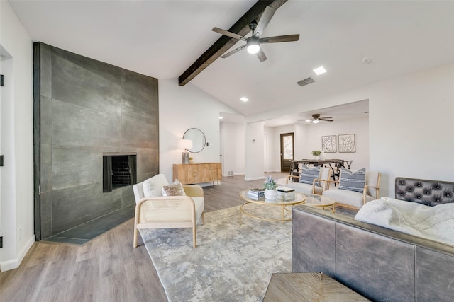 living room with light hardwood / wood-style flooring, vaulted ceiling with beams, ceiling fan, and a large fireplace