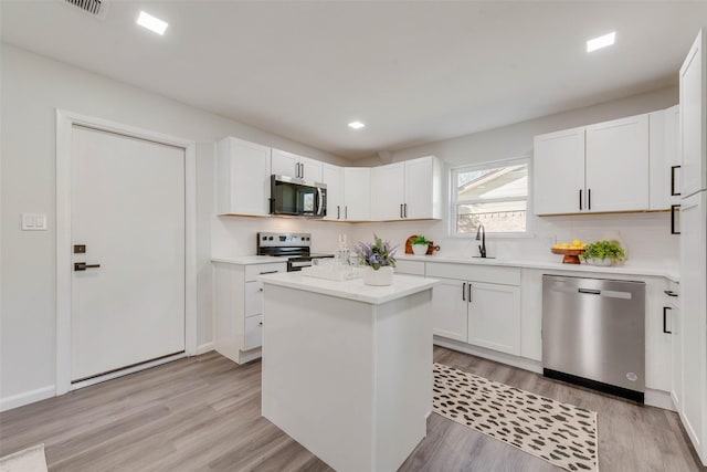 kitchen featuring appliances with stainless steel finishes, sink, white cabinets, light wood-type flooring, and a center island