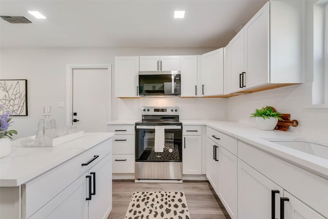 kitchen with light stone countertops, white cabinetry, stainless steel appliances, and light wood-type flooring