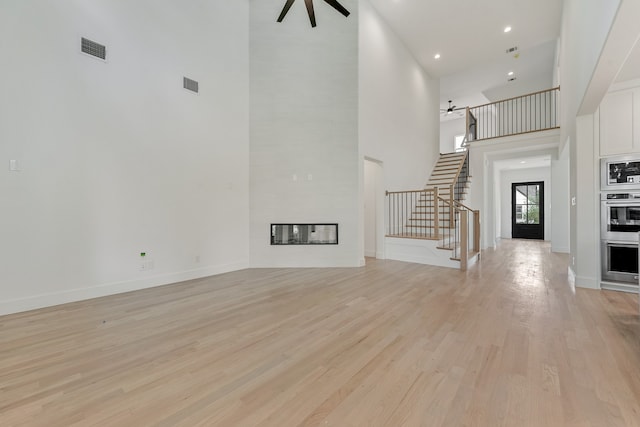 unfurnished living room with ceiling fan, a fireplace, light hardwood / wood-style floors, and a towering ceiling