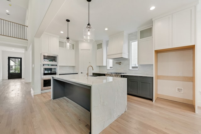 kitchen with a kitchen island with sink, built in microwave, white cabinets, and premium range hood