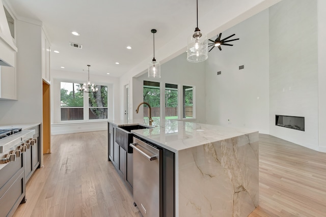 kitchen featuring stainless steel appliances, a spacious island, a fireplace, light stone countertops, and white cabinets