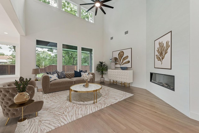 living room with ceiling fan, a towering ceiling, and light hardwood / wood-style floors