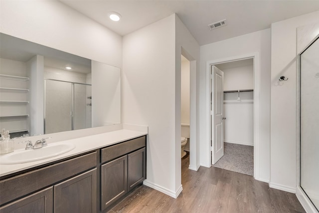 bathroom featuring hardwood / wood-style flooring, toilet, a shower with shower door, and vanity