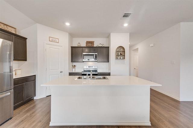 kitchen featuring wood-type flooring, a kitchen island with sink, dark brown cabinetry, and appliances with stainless steel finishes