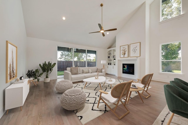 living room featuring built in features, high vaulted ceiling, ceiling fan, and light wood-type flooring