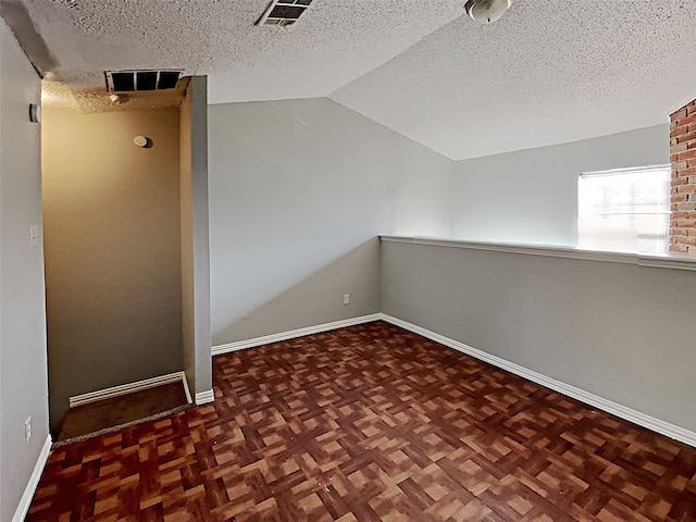 unfurnished room featuring a textured ceiling, dark parquet flooring, and vaulted ceiling