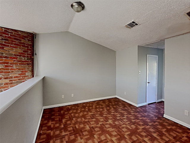 spare room featuring vaulted ceiling, dark parquet floors, and a textured ceiling