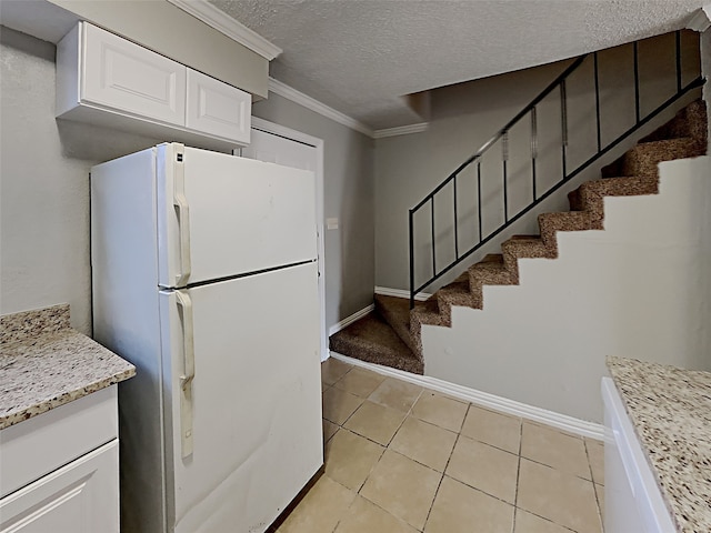 kitchen with light stone counters, a textured ceiling, crown molding, white refrigerator, and white cabinetry