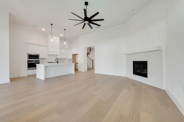 unfurnished living room with light hardwood / wood-style flooring, a brick fireplace, ceiling fan, and sink