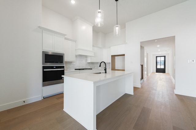 kitchen featuring built in microwave, a kitchen island with sink, sink, white cabinets, and oven