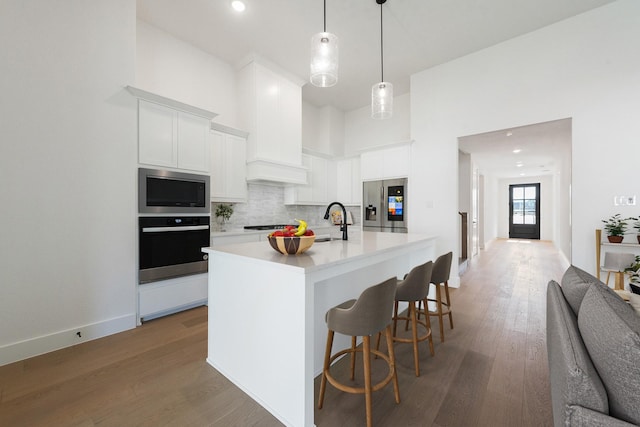 kitchen featuring appliances with stainless steel finishes, white cabinetry, hanging light fixtures, tasteful backsplash, and an island with sink