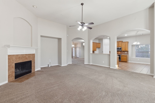 unfurnished living room with a fireplace, light carpet, and ceiling fan with notable chandelier