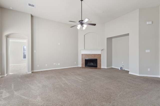 unfurnished living room with a tiled fireplace, ceiling fan, carpet, and a high ceiling