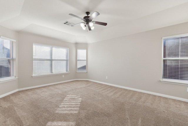 empty room featuring ceiling fan, a raised ceiling, and light colored carpet