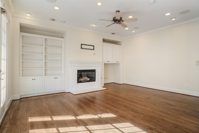 unfurnished living room featuring built in shelves, ceiling fan, wood-type flooring, and crown molding