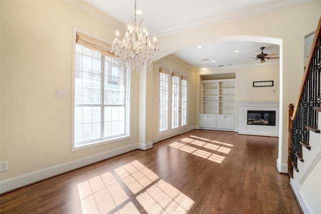 unfurnished living room with built in shelves, dark hardwood / wood-style floors, ornamental molding, and ceiling fan with notable chandelier