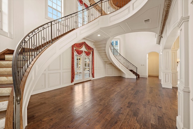 interior space with dark wood-type flooring, a towering ceiling, and decorative columns